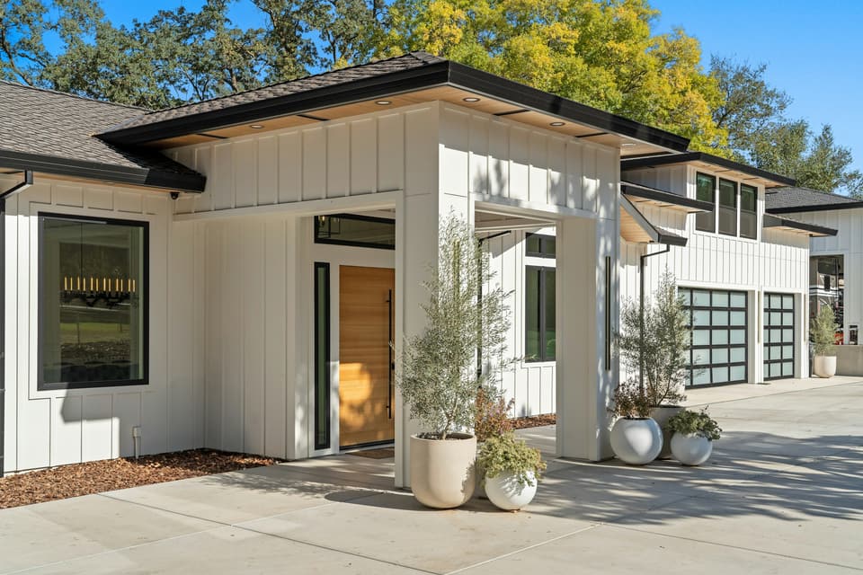 A modern white house with black-framed glass garage doors and potted olive trees