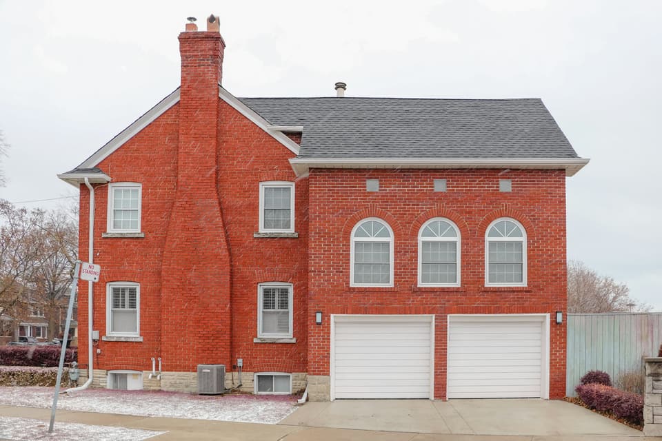 A red brick two-story house with two white garage doors