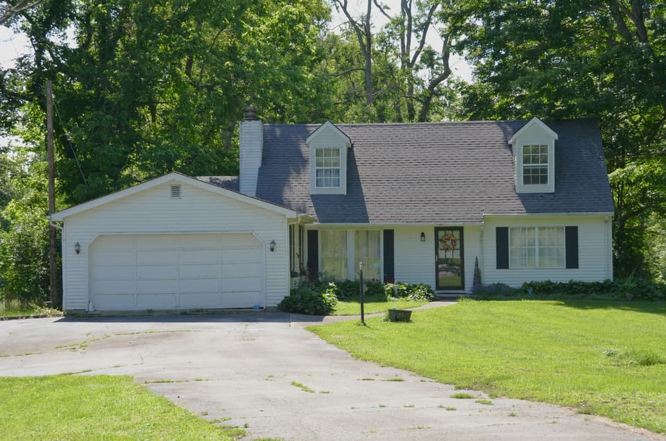 A white house with an attached garage, a driveway and a green lawn